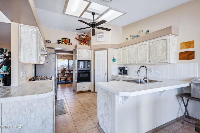 kitchen featuring a sink, tile counters, a ceiling fan, and a peninsula