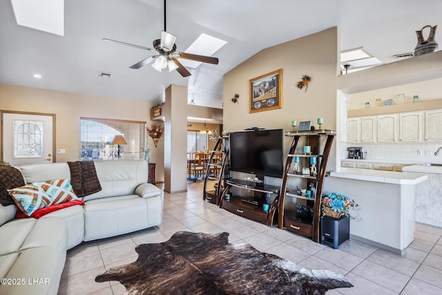 living area featuring visible vents, lofted ceiling with skylight, ceiling fan with notable chandelier, and light tile patterned floors