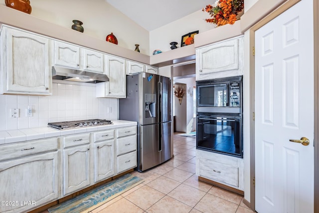 kitchen with tile counters, light tile patterned floors, tasteful backsplash, under cabinet range hood, and black appliances