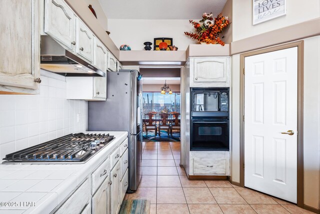 kitchen featuring tile counters, white cabinetry, tasteful backsplash, under cabinet range hood, and black appliances
