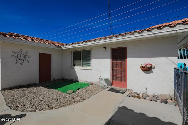 doorway to property featuring a patio area, a tile roof, and fence