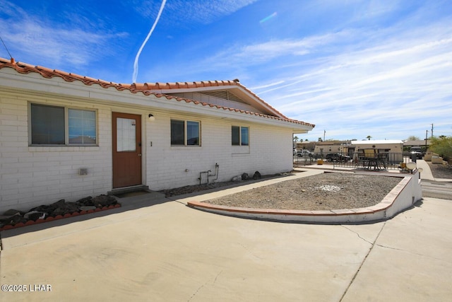 exterior space with a patio area, a tiled roof, fence, and brick siding