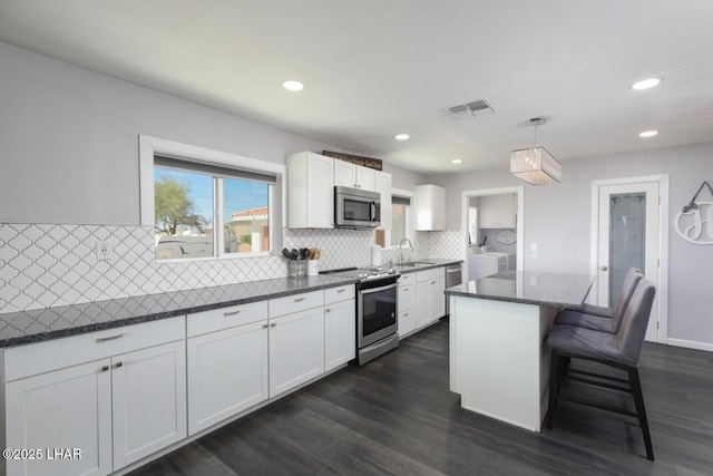 kitchen featuring stainless steel appliances, a kitchen island, visible vents, white cabinets, and dark stone counters