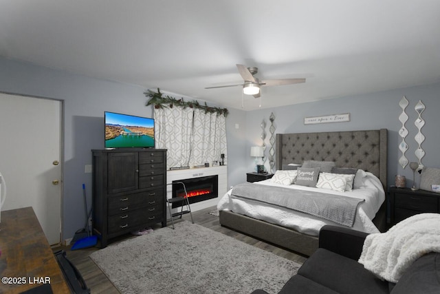 bedroom featuring dark wood-style floors, a ceiling fan, and a glass covered fireplace