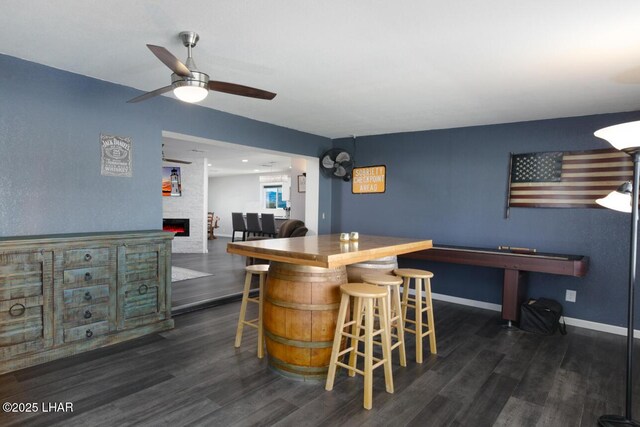 bar with dark wood-style floors, a fireplace, baseboards, and a ceiling fan