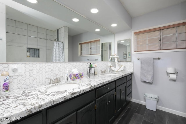 full bath with double vanity, tasteful backsplash, a sink, and baseboards