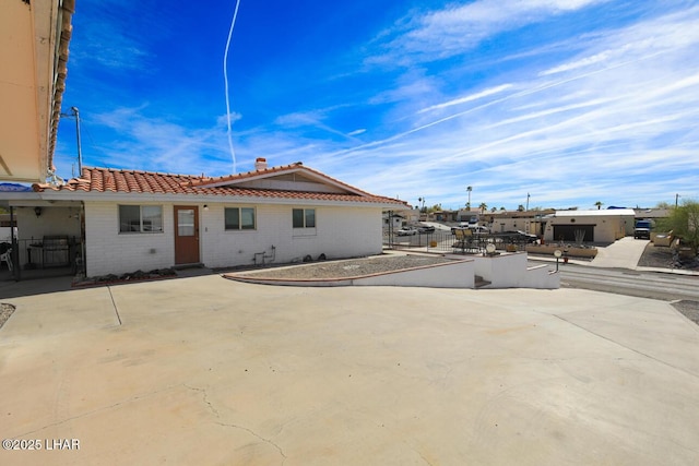 back of property featuring brick siding, a tile roof, fence, and a patio