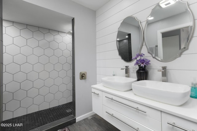 full bathroom featuring wood finished floors, double vanity, a sink, and a walk in shower