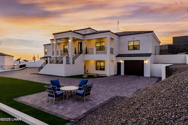 back house at dusk featuring a garage, a balcony, and a patio area