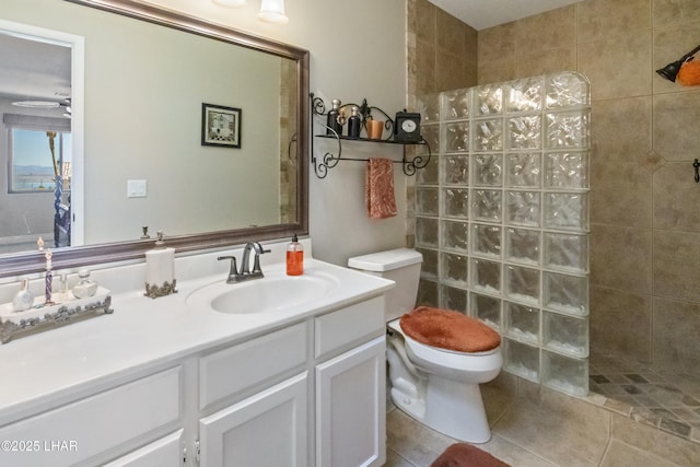 bathroom with toilet, a tile shower, tile patterned flooring, and vanity