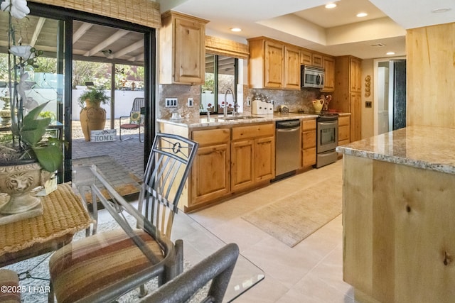 kitchen with tasteful backsplash, stainless steel appliances, light stone counters, light tile patterned floors, and sink