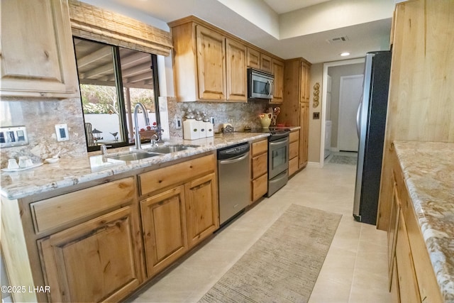 kitchen with appliances with stainless steel finishes, light stone counters, backsplash, light tile patterned floors, and sink