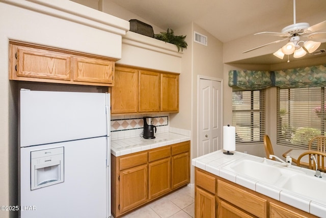 kitchen featuring light tile patterned flooring, tile countertops, sink, white fridge with ice dispenser, and ceiling fan