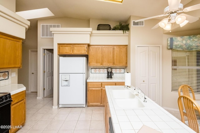 kitchen featuring light tile patterned flooring, sink, decorative backsplash, white refrigerator, and tile counters