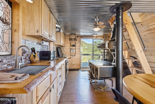 kitchen with dark hardwood / wood-style floors, light brown cabinetry, tasteful backsplash, sink, and a wood stove