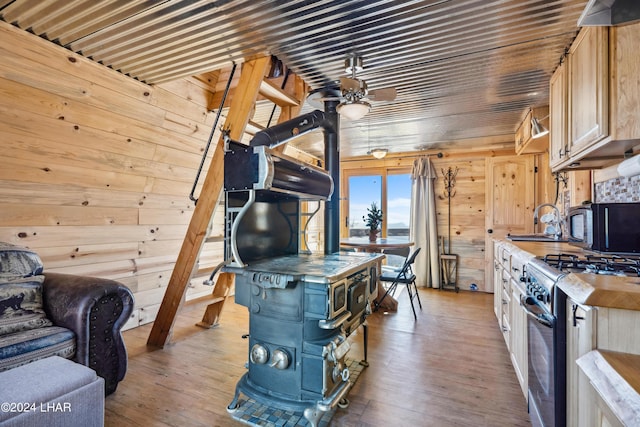 kitchen featuring a wood stove, wood walls, stainless steel gas range oven, light brown cabinets, and light wood-type flooring