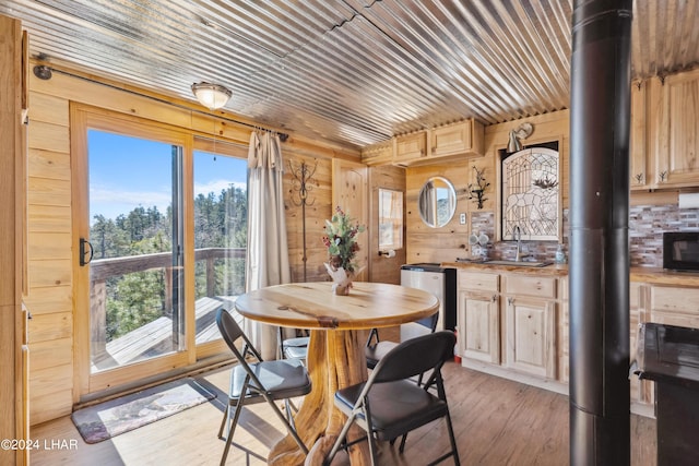 dining area with sink, wood walls, light hardwood / wood-style flooring, wooden ceiling, and a wood stove