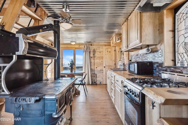 kitchen featuring ceiling fan, decorative backsplash, gas range, light wood-type flooring, and a wood stove