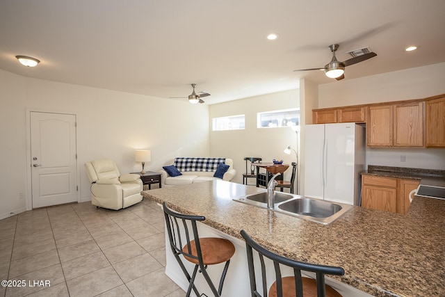 kitchen with sink, light tile patterned floors, ceiling fan, white refrigerator, and a kitchen bar