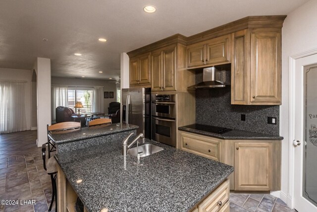 kitchen featuring a kitchen island with sink, backsplash, stainless steel appliances, and wall chimney exhaust hood