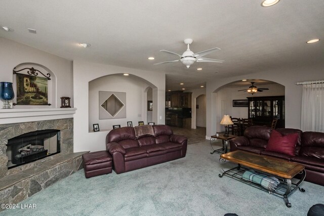 living room with a stone fireplace, carpet floors, and ceiling fan
