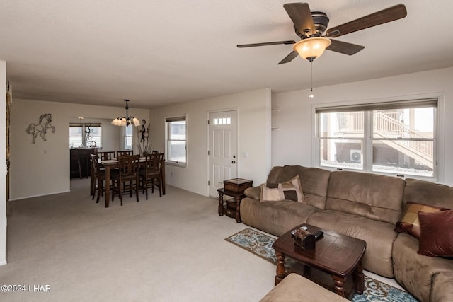 living area with ceiling fan with notable chandelier, light colored carpet, and a healthy amount of sunlight