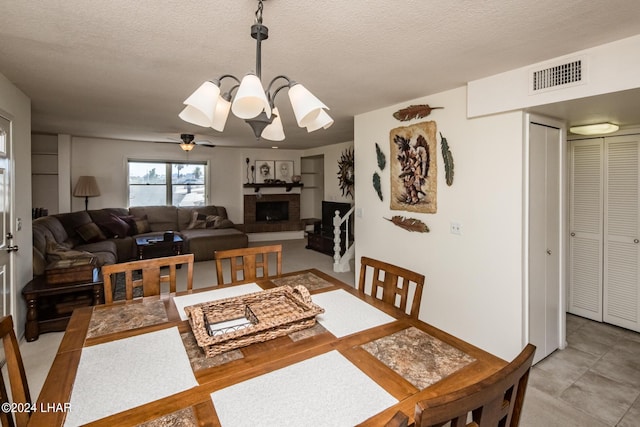 dining area with a textured ceiling, ceiling fan with notable chandelier, a brick fireplace, and visible vents