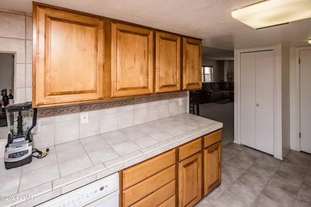 kitchen featuring tasteful backsplash, dishwashing machine, tile countertops, and brown cabinets