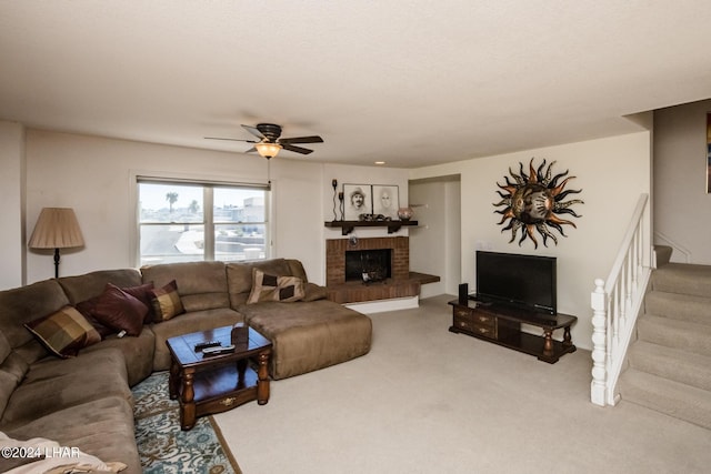 carpeted living area with ceiling fan, a brick fireplace, and stairs