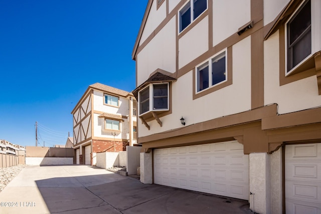 view of side of home with concrete driveway, stucco siding, fence, and an attached garage