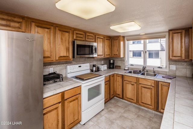 kitchen with tile countertops, brown cabinetry, tasteful backsplash, appliances with stainless steel finishes, and a sink