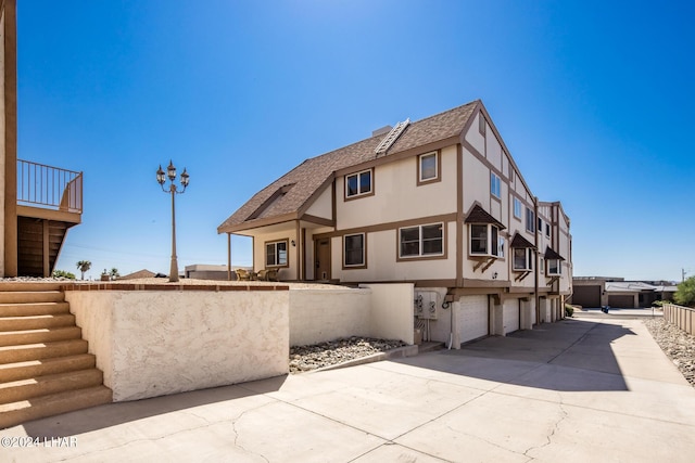 view of front facade with stucco siding, stairway, driveway, an attached garage, and fence