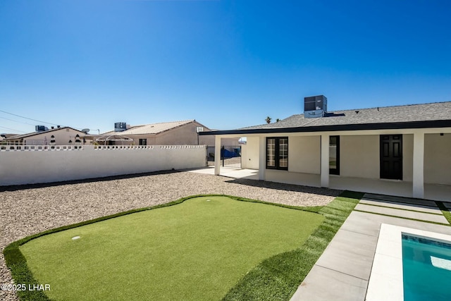 back of house with a fenced backyard, central air condition unit, roof with shingles, stucco siding, and a patio area