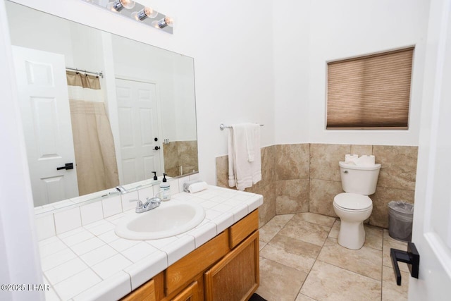 bathroom with vanity, a wainscoted wall, tile patterned flooring, tile walls, and toilet