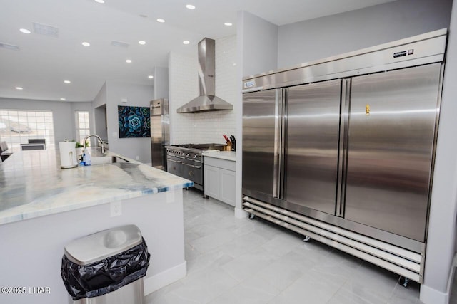 kitchen with light stone countertops, a sink, wall chimney range hood, premium appliances, and backsplash