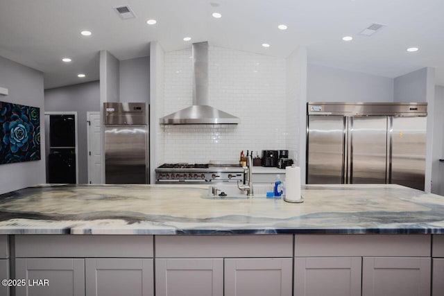 kitchen featuring visible vents, light stone countertops, high end appliances, and wall chimney exhaust hood