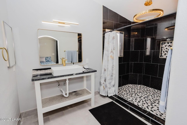 bathroom with tile patterned floors, tiled shower, baseboards, and a sink