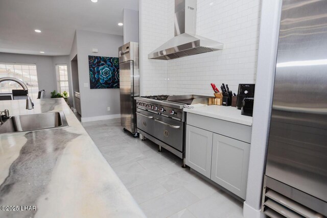 kitchen with a sink, backsplash, stainless steel appliances, wall chimney exhaust hood, and light countertops