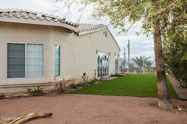 view of property exterior featuring a tiled roof, stucco siding, a yard, and fence