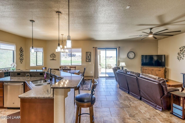 kitchen featuring sink, a kitchen breakfast bar, dark stone counters, hanging light fixtures, and stainless steel dishwasher