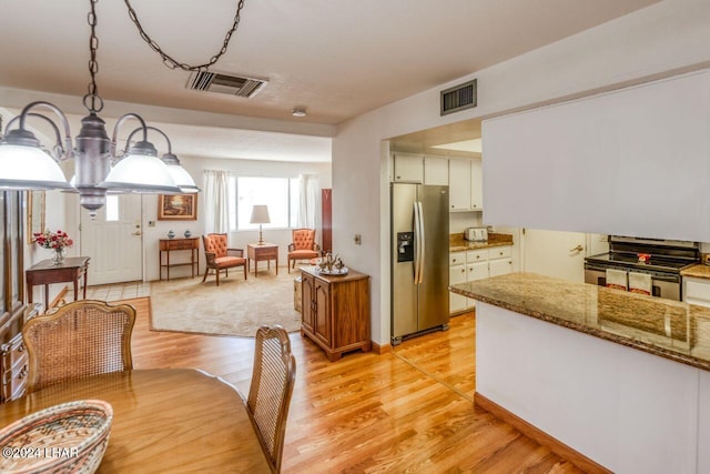 kitchen with white cabinets, hanging light fixtures, light stone counters, light hardwood / wood-style floors, and stainless steel appliances