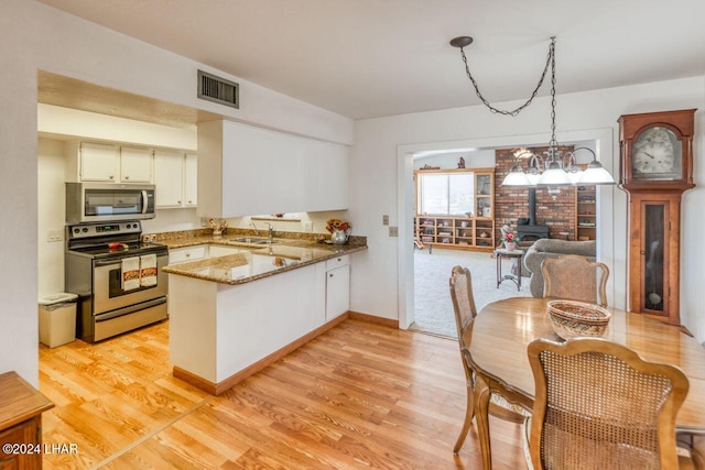 kitchen featuring decorative light fixtures, a wood stove, kitchen peninsula, stainless steel appliances, and light stone countertops