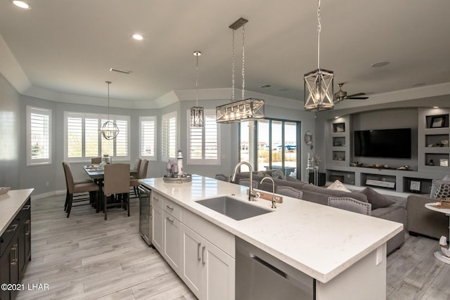 kitchen with pendant lighting, an island with sink, sink, white cabinets, and stainless steel dishwasher