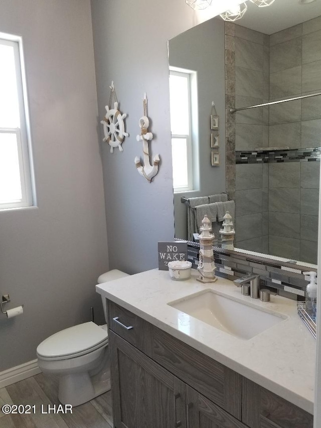 bathroom featuring hardwood / wood-style flooring, tiled shower, vanity, and toilet