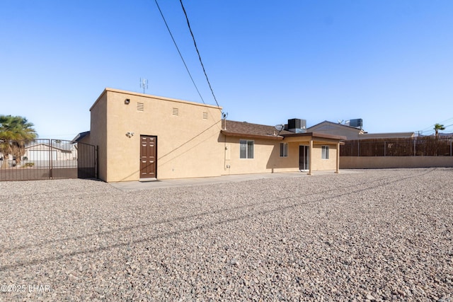 rear view of house with fence, cooling unit, and stucco siding