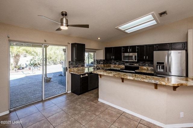 kitchen featuring vaulted ceiling, decorative backsplash, a breakfast bar area, dark cabinetry, and appliances with stainless steel finishes