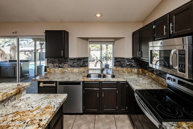 kitchen featuring tasteful backsplash, a sink, dark cabinetry, stainless steel appliances, and light stone countertops