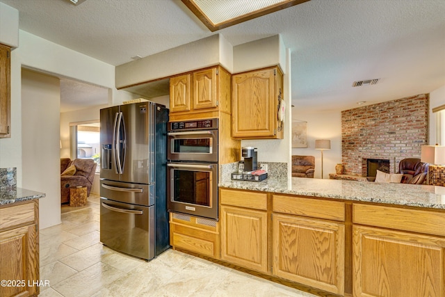 kitchen featuring light stone counters, stainless steel fridge with ice dispenser, a brick fireplace, a textured ceiling, and double oven