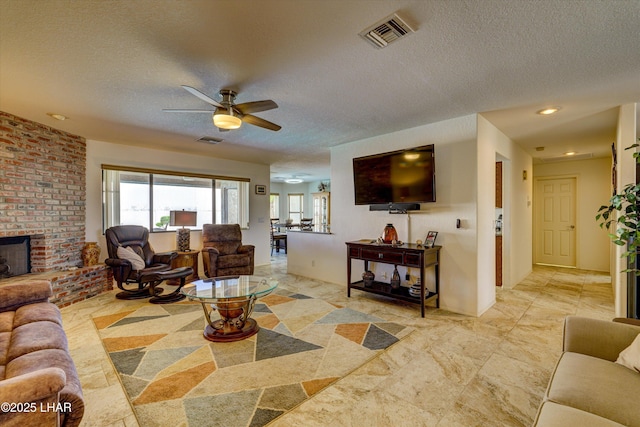 living room featuring ceiling fan, a fireplace, and a textured ceiling