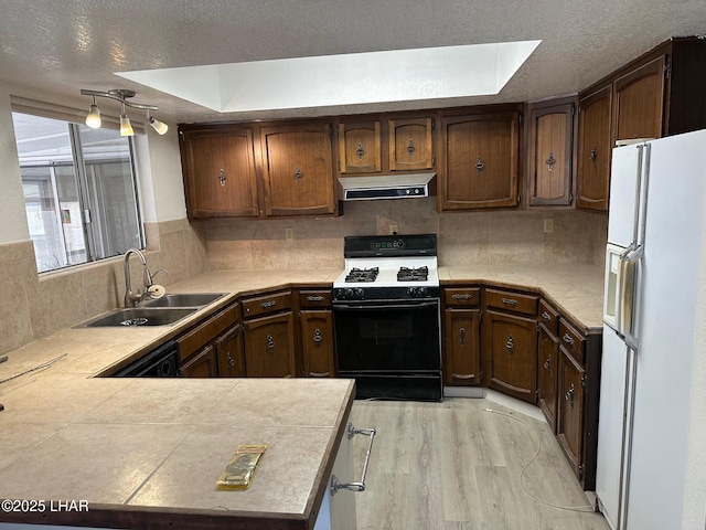 kitchen with sink, gas range oven, kitchen peninsula, white refrigerator with ice dispenser, and decorative backsplash